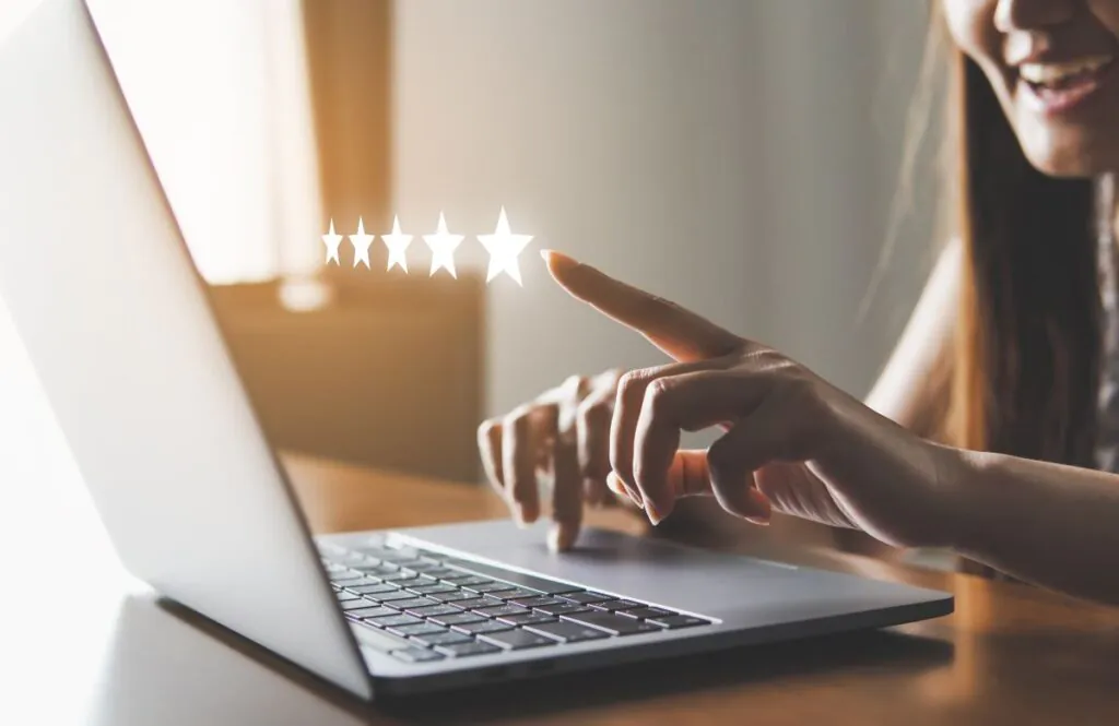 Person smiling and looking at a laptop pointing at a hologram of a 5 star review