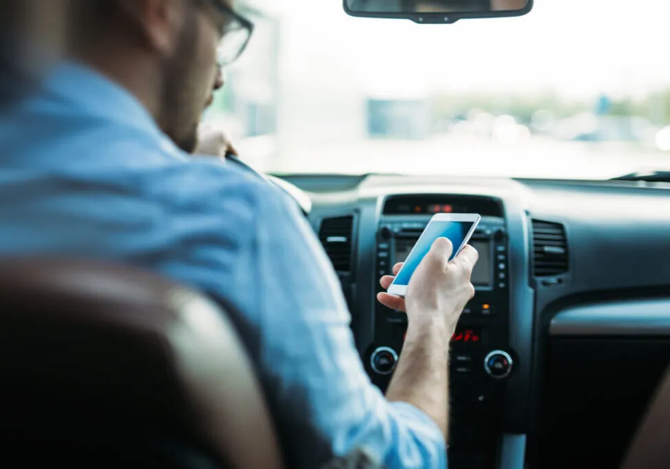 Image of a man driving a car while looking at cellphone