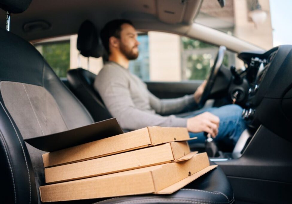 July_Delivery_use Man driving a car with pizza boxes in the passenger seat