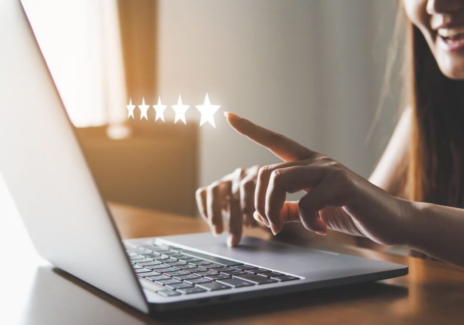 Reviews Person smiling and looking at a laptop pointing at a hologram of a 5 star review