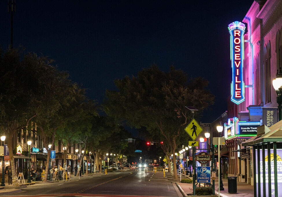 Roseville Downtown Image of downtown Roseville, CA with local theater's neon sign lit up and people talking on a sidewalk