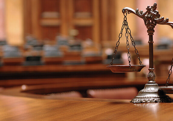 penney-assoc-justice-scales-courtroom Justice scales sitting on a courtroom desk
