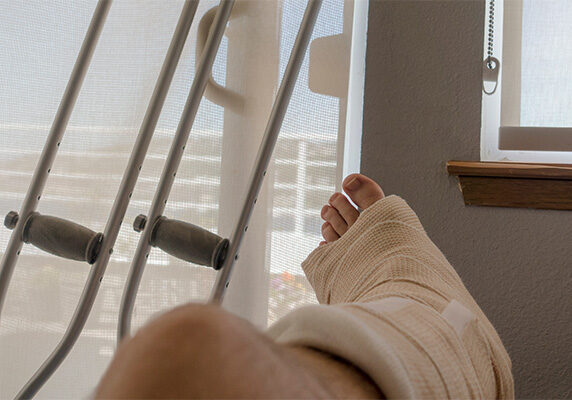 Person's leg in hard cast with crutches leaning on a window