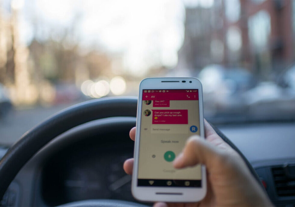 Person holding phone in front of steering wheel and texting
