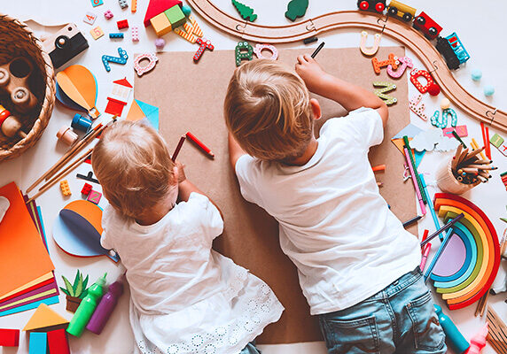 Children laying on ground and coloring while surrounded by toys