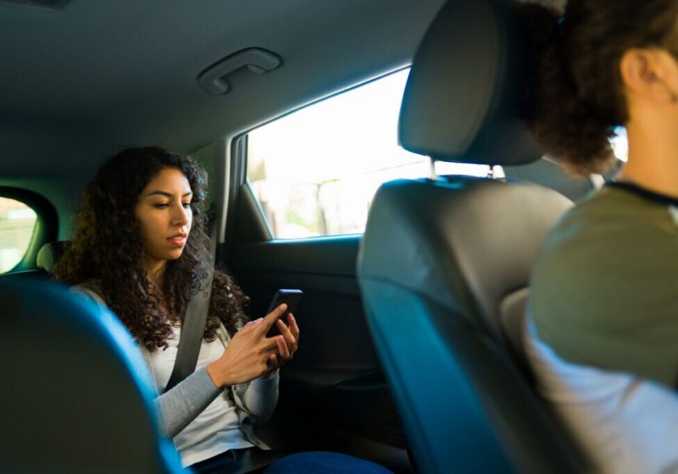 Woman in the back of a car, sitting behind the driver, while on her phone